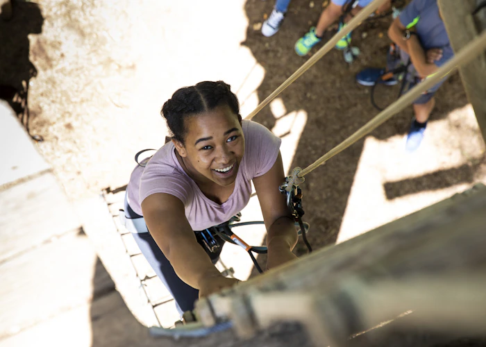Young person climbs a ladder on a high ropes course.