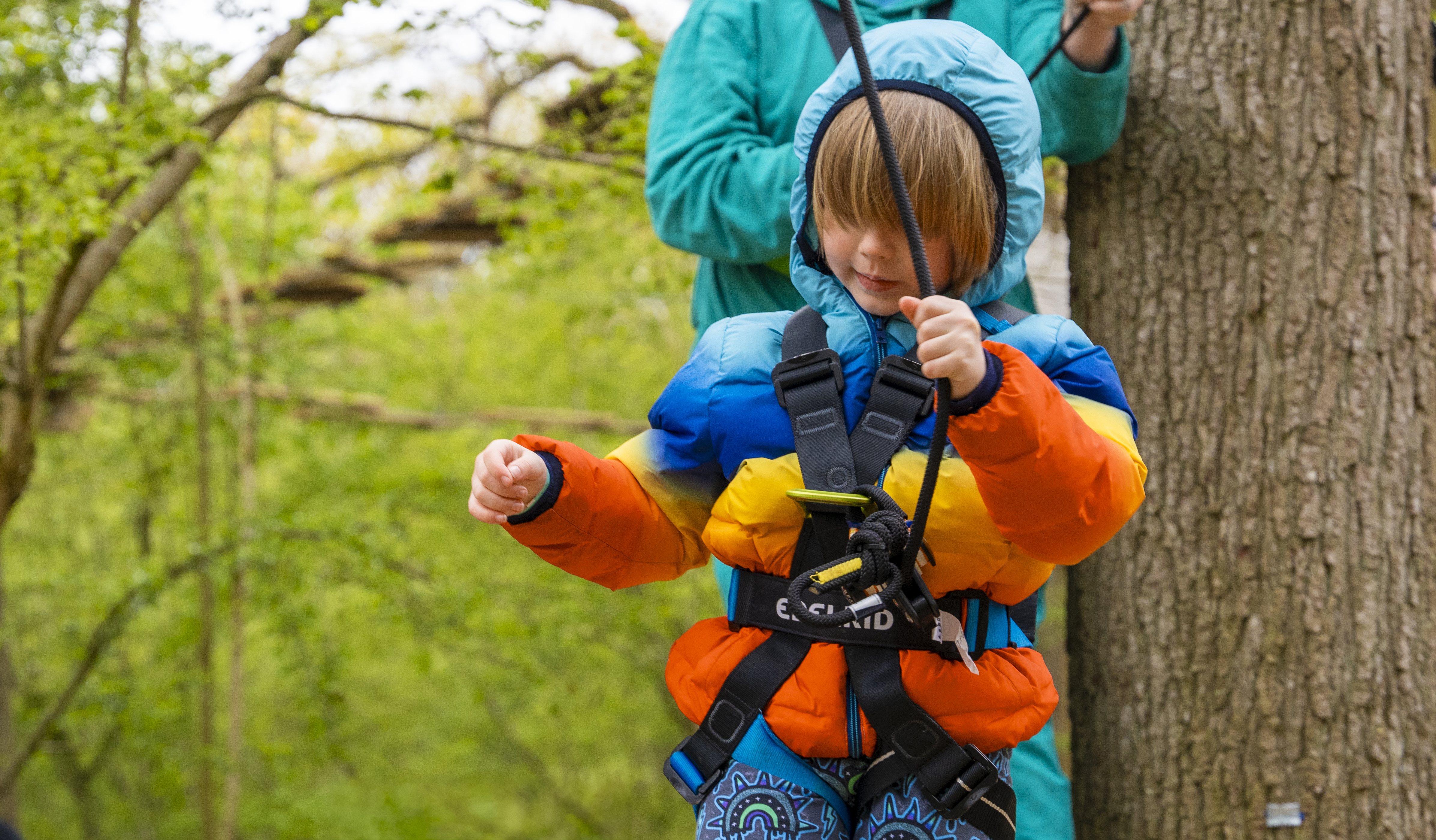 Young person on a high ropes course wearing a harness.