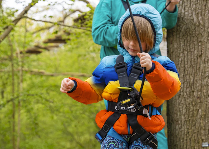 Young person on a high ropes course wearing a harness.