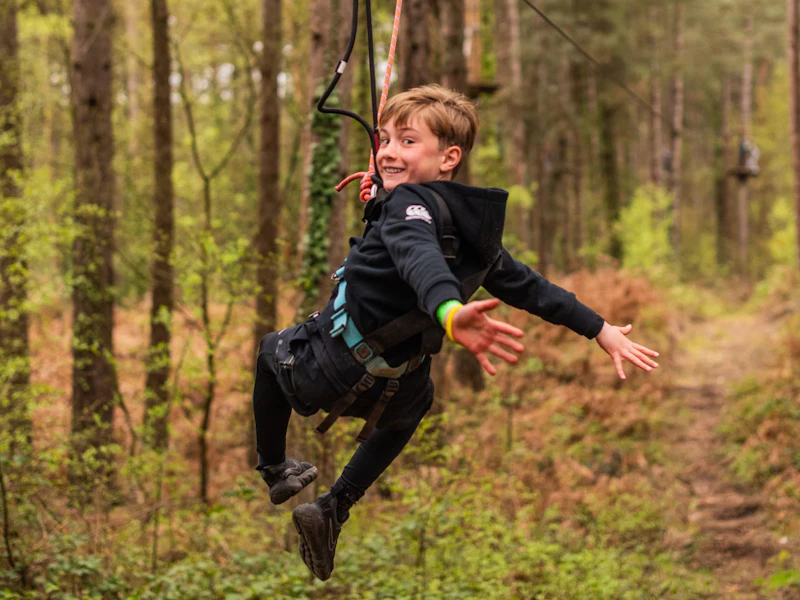 Boy on Treetop Adventure Plus Zip Wire A boy with his arms stretched out and smiling as he rides a zip wire through the forest