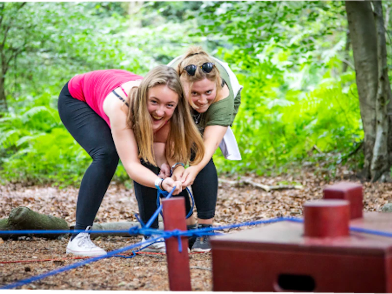 Isotope team game Two women crouch and pull on a length of elastic for a Go Ape team game in the forest