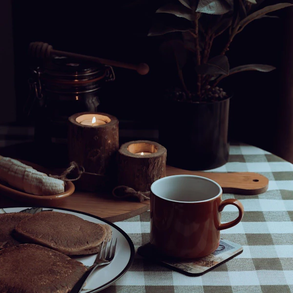 A coffee cup and a plate of pancakes sit on a table in a rustic cafe