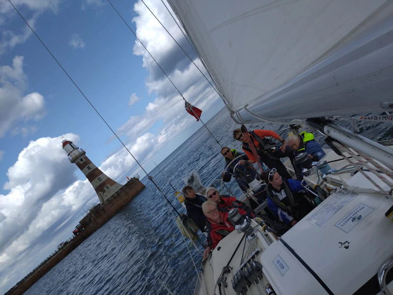 AdventureMind Grant 2025 A group on a sailing boat with a lighthouse behind them.