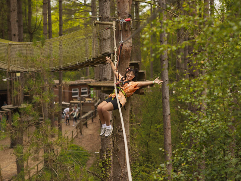 Girl on crossing A girl wearing an orange t-shirt throws her arms out as she zips of a high ropes crossing
