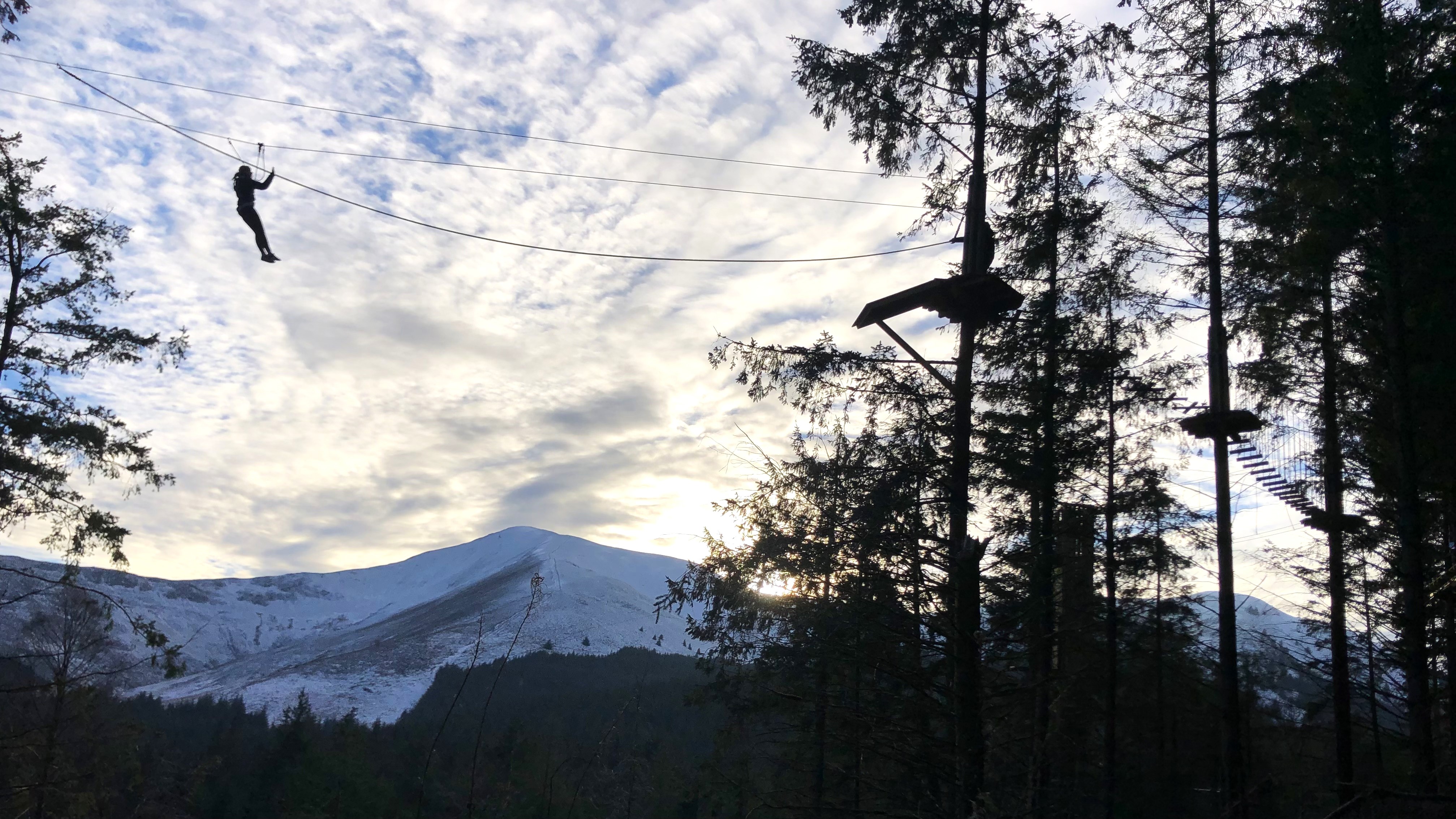 Silhouette of a person on a zipline with mountain scenery in the background.