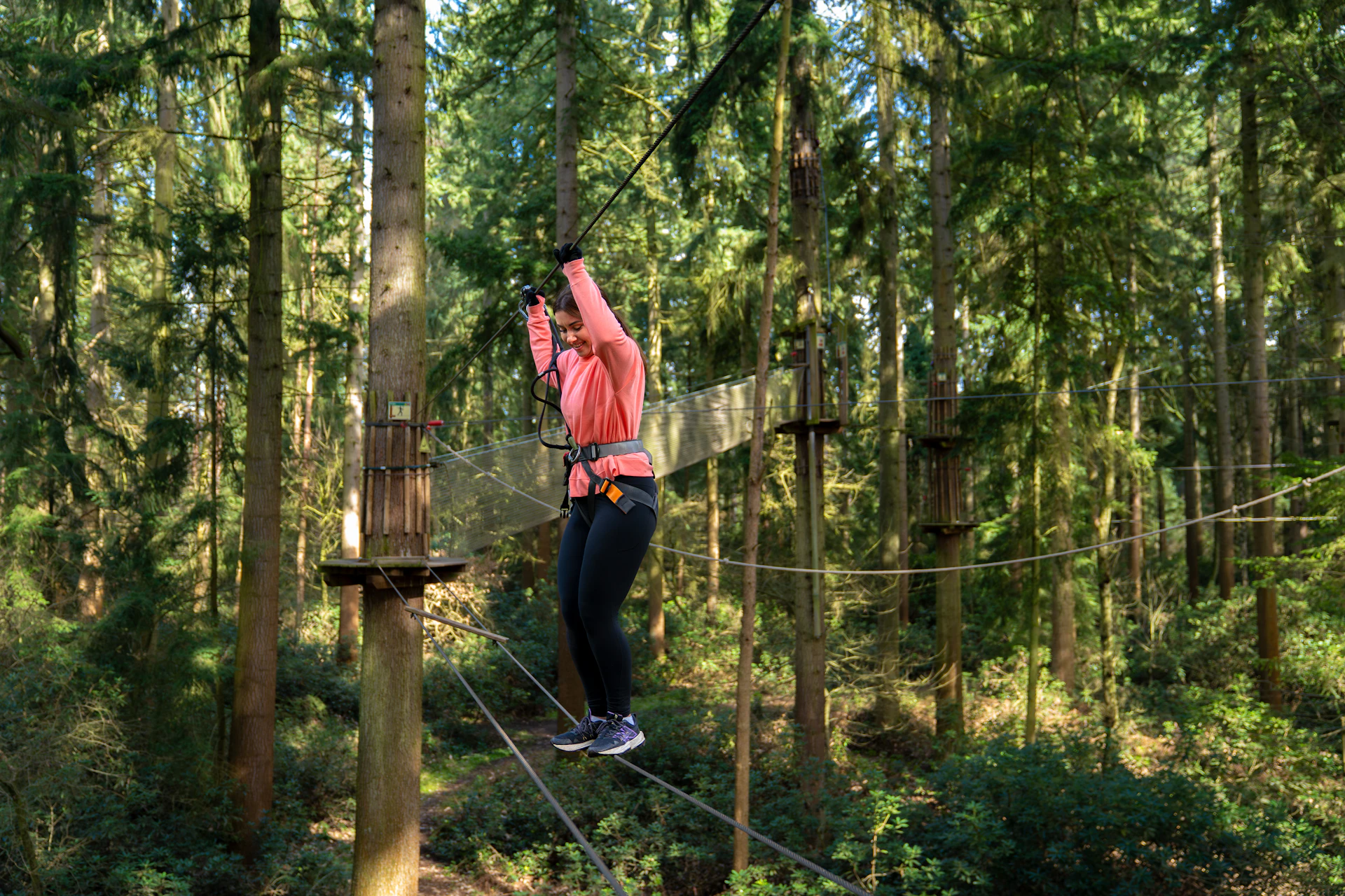 A woman shuffles her way over a high ropes crossing on a forest adventure