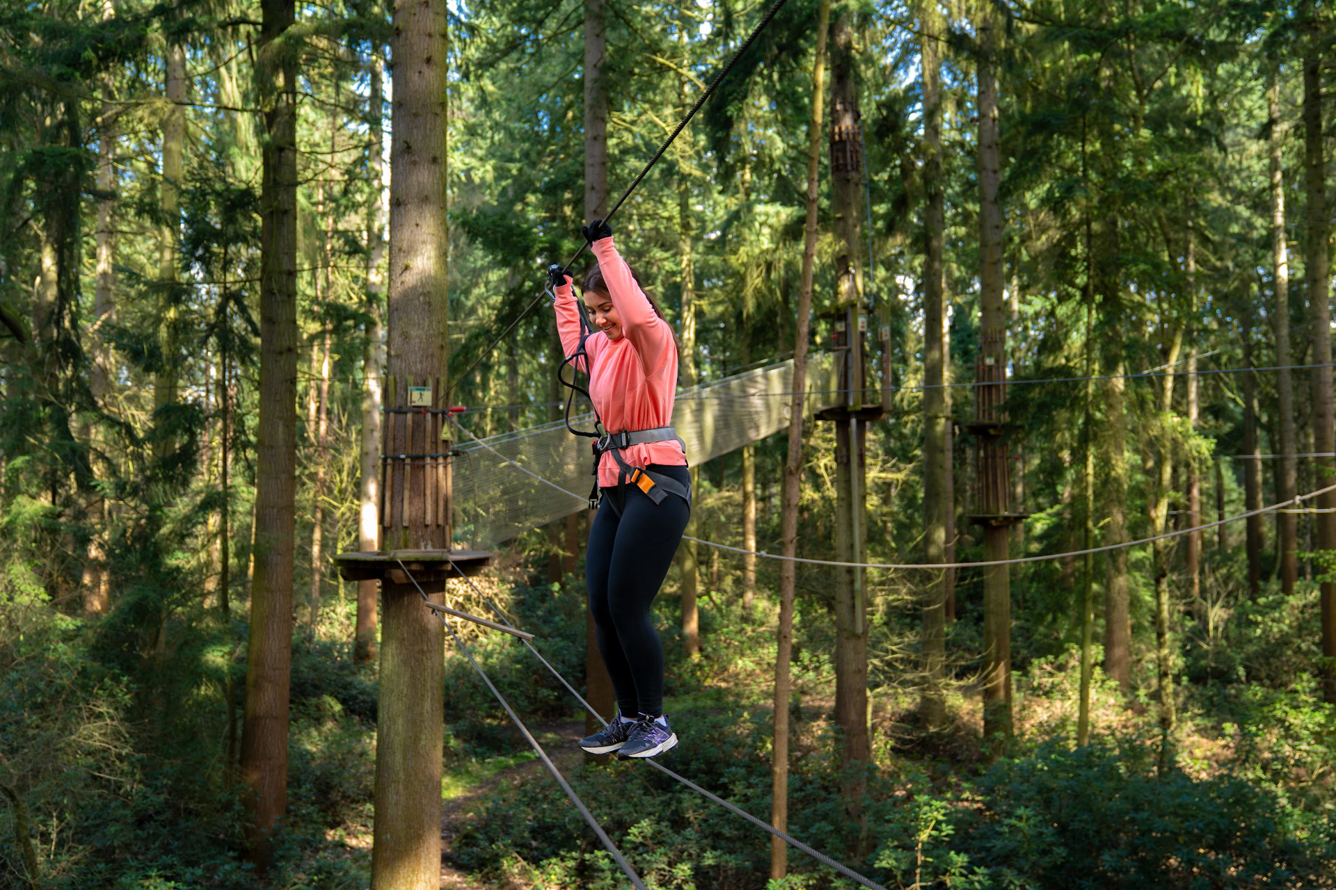 A woman smiles as she shuffles over a high ropes crossing on a forest adventure