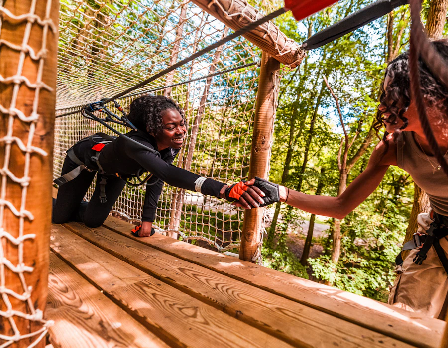 A women helps her friend as she climbs through a Net Tunnel crossing in the treetops
