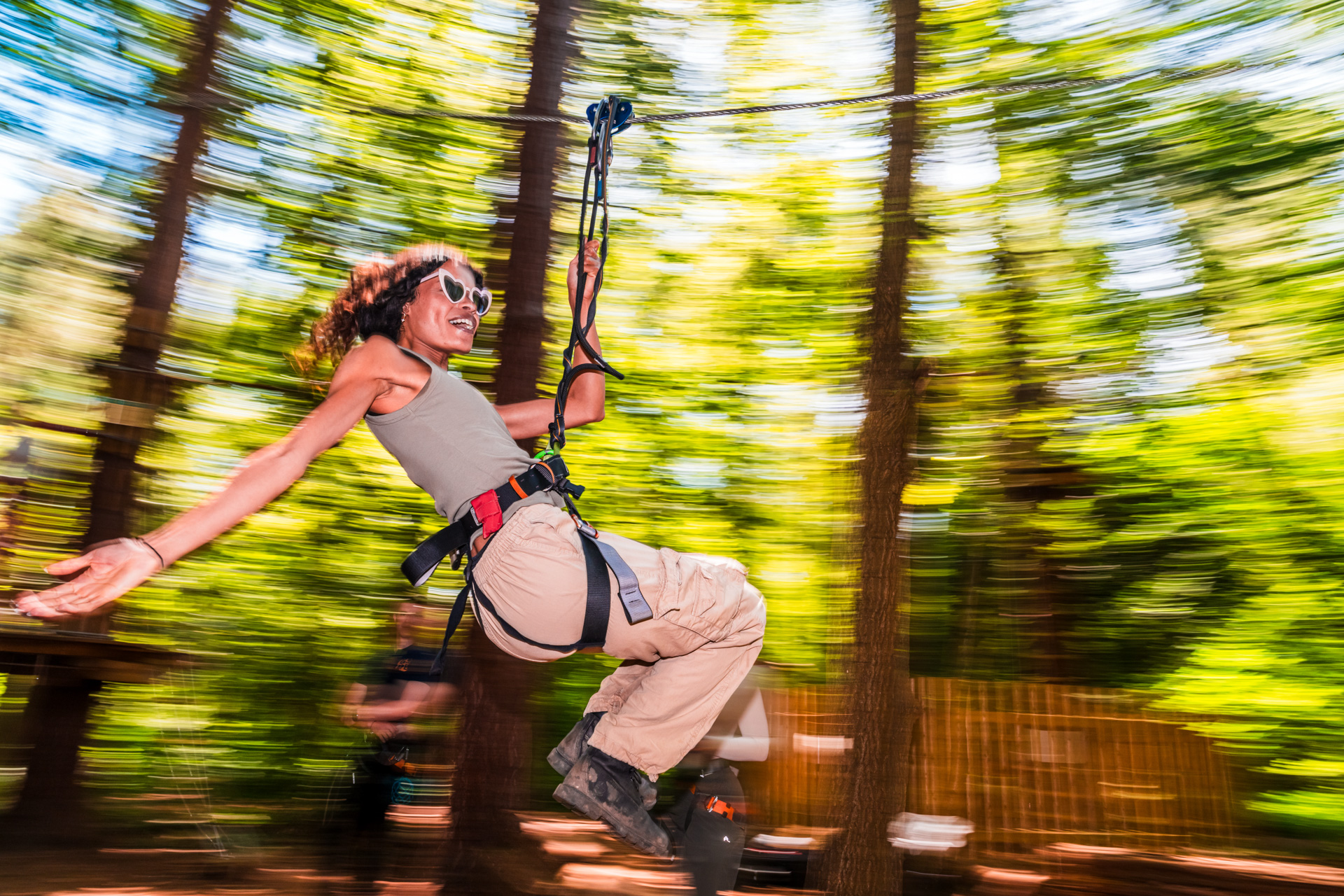 A woman holds out her arm as she rides a zip wir eon a sunny day