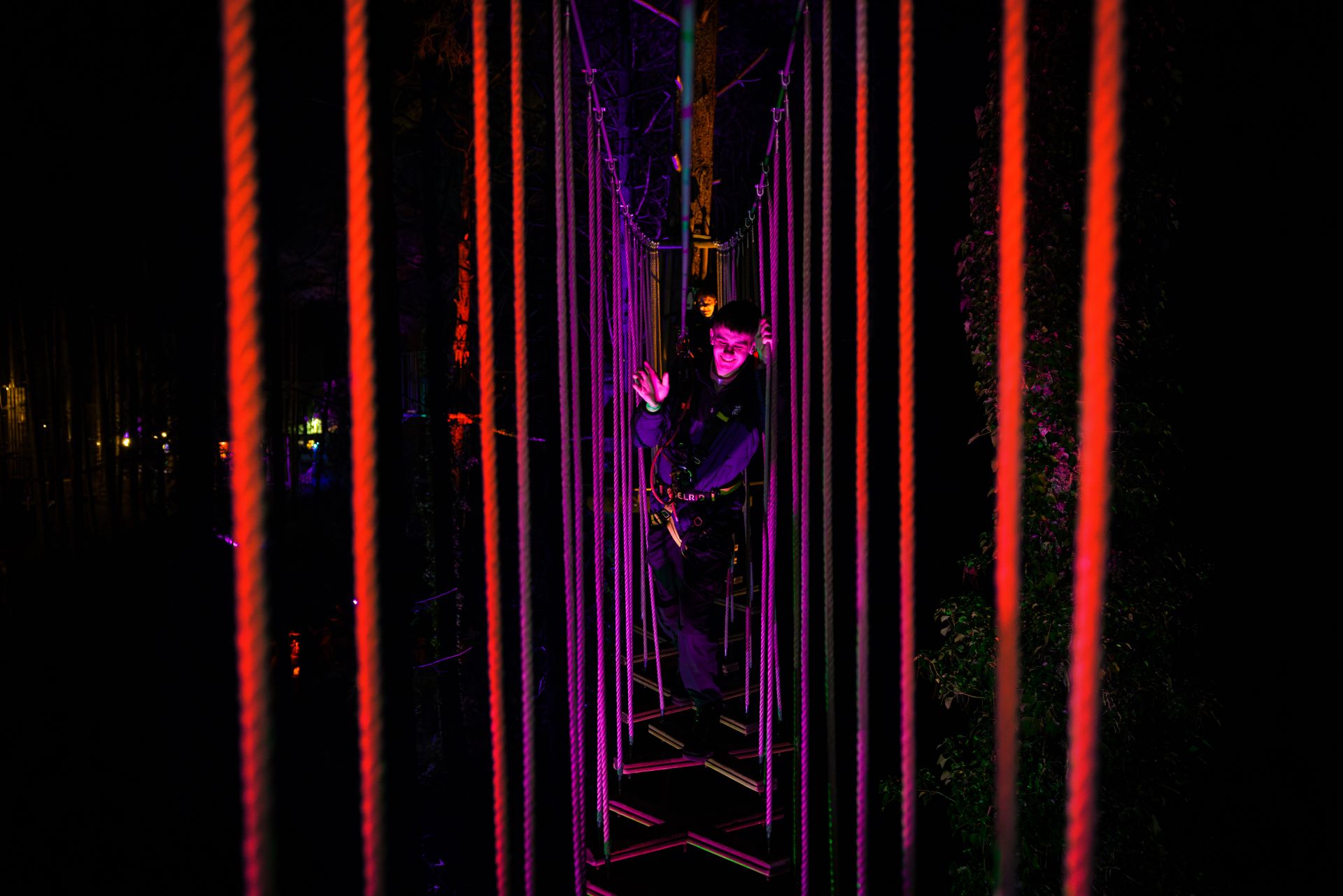 A young man smiles as he navigates a wobbly Go Ape crossing in the dark