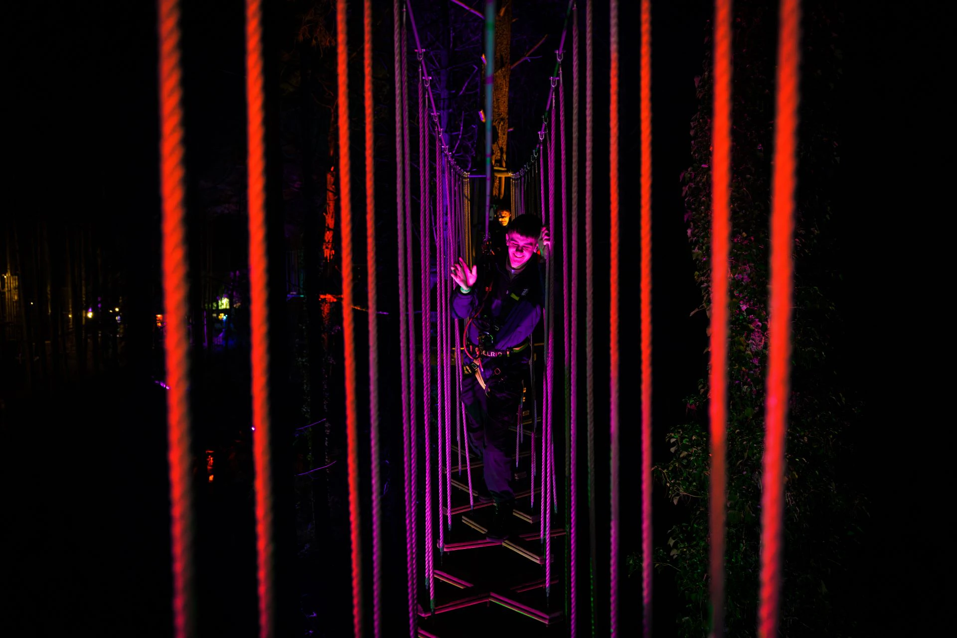 A young man smiles as he navigates a wobbly Go Ape crossing in the dark