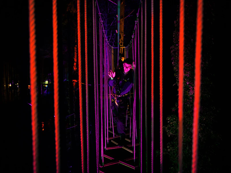 Sundown Adventures Crossed Wires A young man smiles as he navigates a wobbly Go Ape crossing in the dark