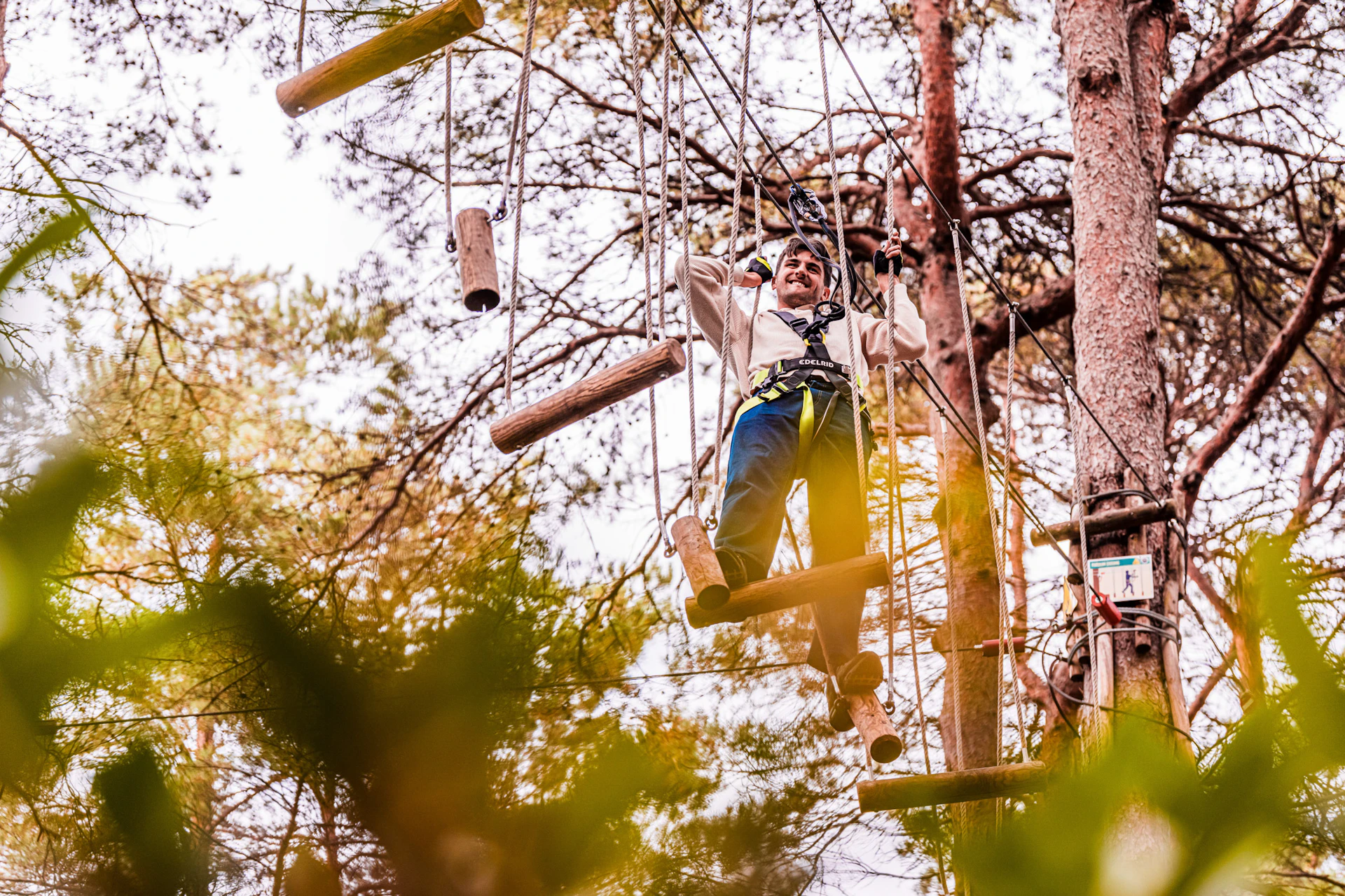 A man works his way over a treetop crossing