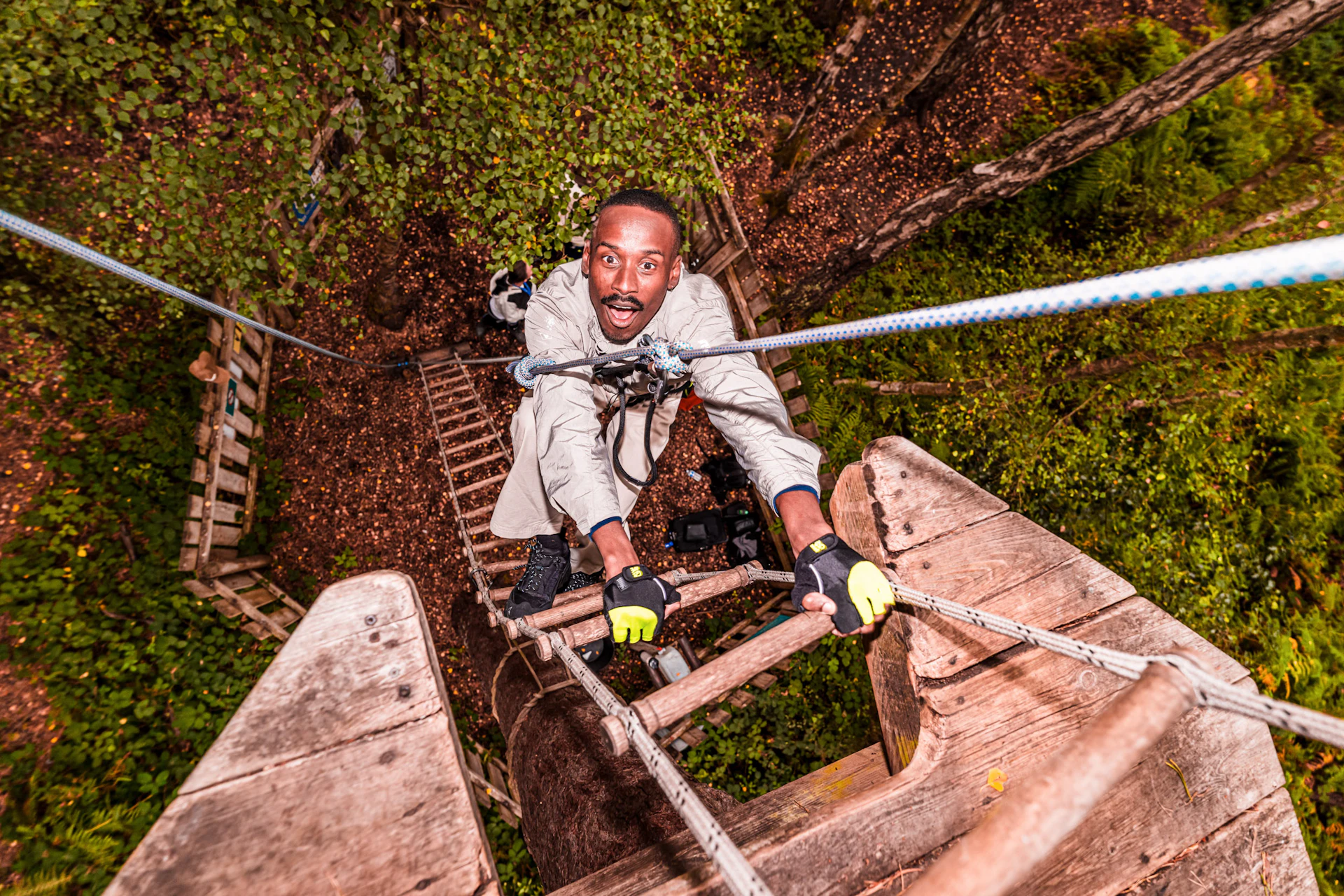 A man grins with excitement as he climbs a rope ladder into the treetops on a day out