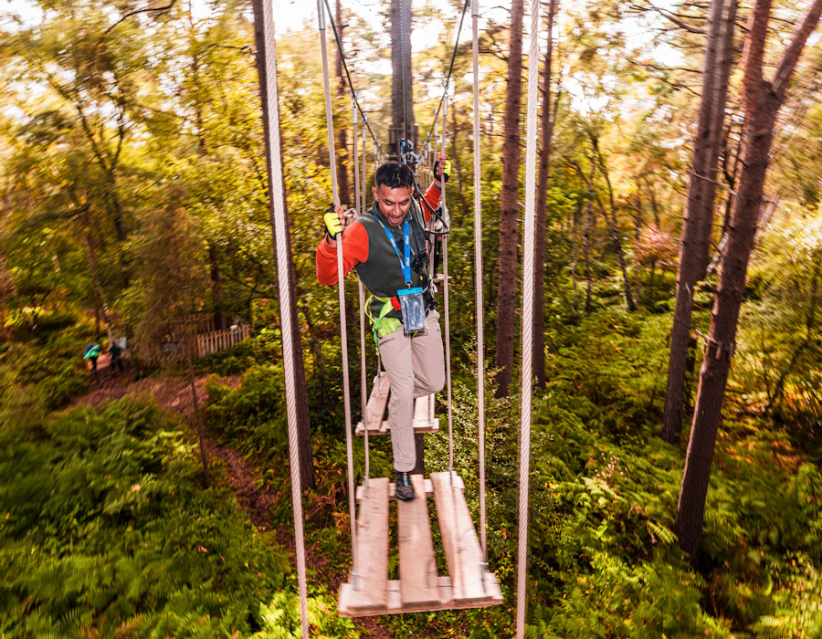 A man makes his way over a wobbly high ropes crossing on a fun day out