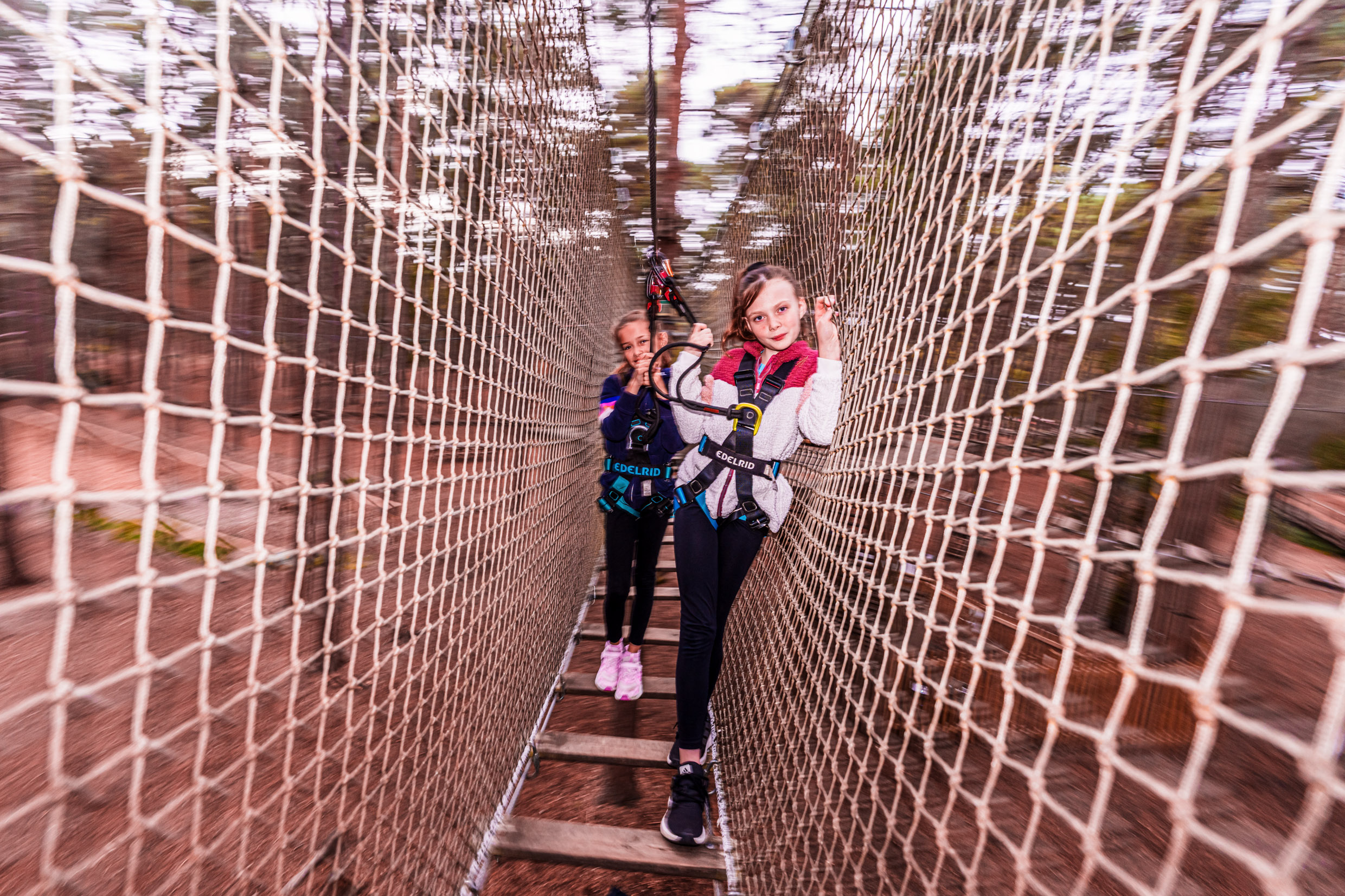 Two girls pose for a photo mid-way through a high ropes crossing at Go Ape