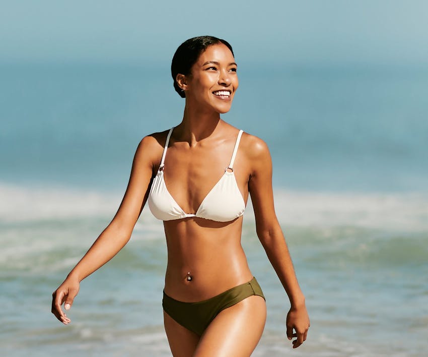 smiling woman in a bikini walking on the beach