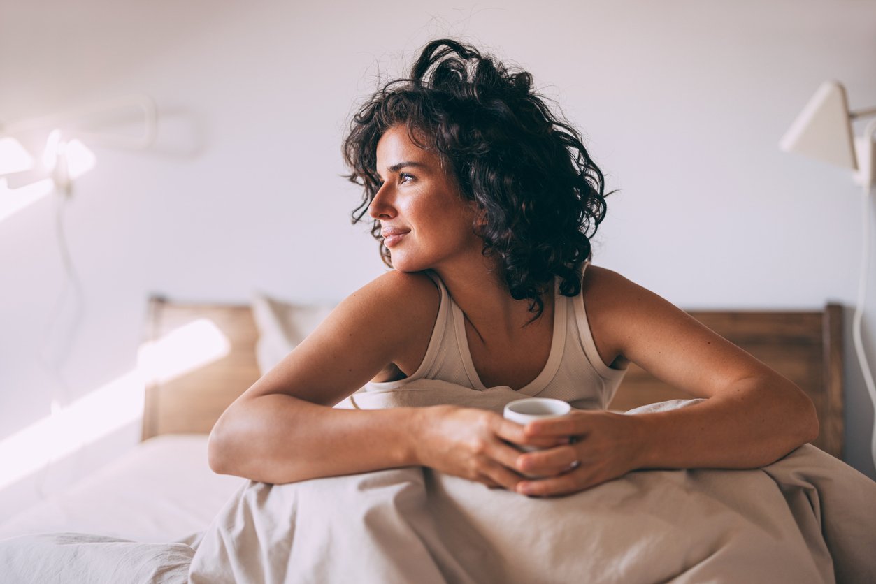 Woman sitting comfortably in bed holding a cup.