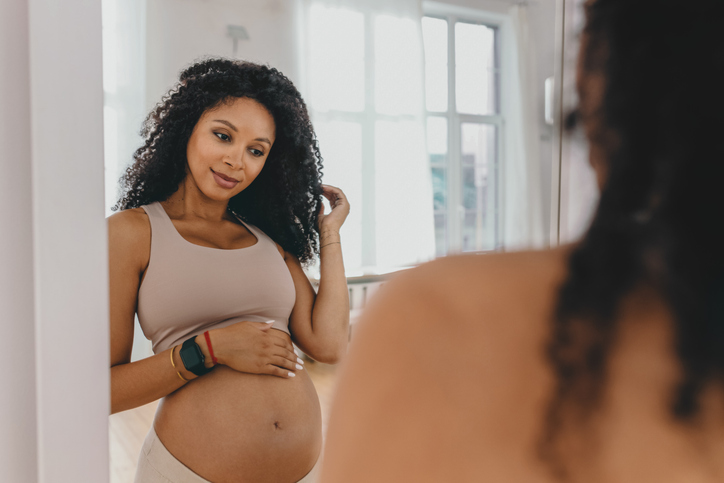Pregnant woman looking at her reflection in a mirror while wearing a sports bra