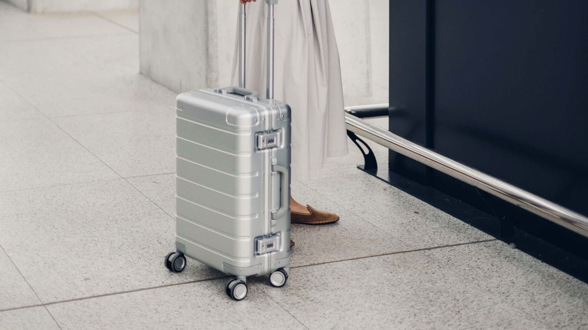 Plan rapproché d'une valise grise aux côtés d'une voyageuse qui fait son enregistrement