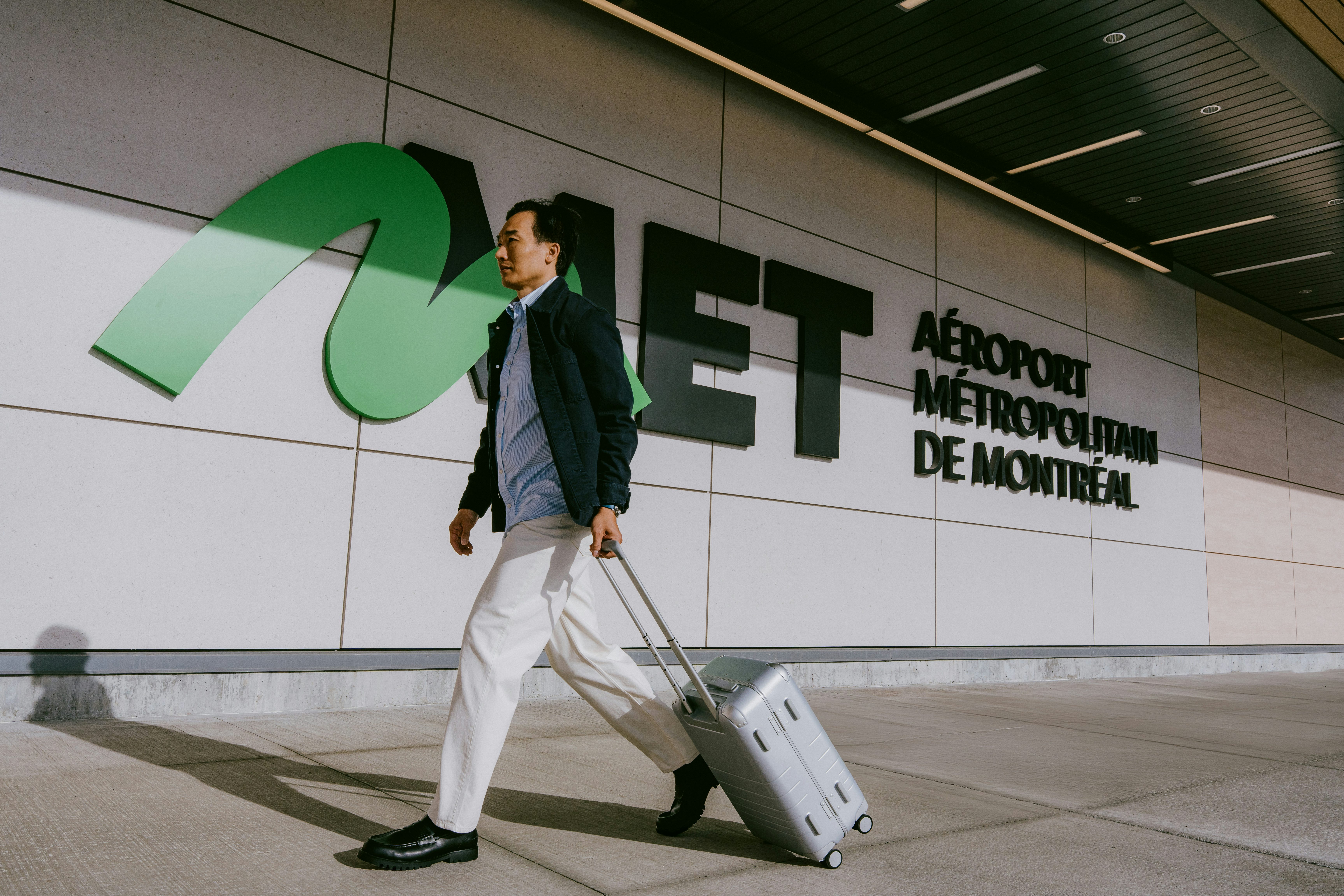Traveler with rolling suitcase in front of the MET – Montréal Metropolitan Airport sign