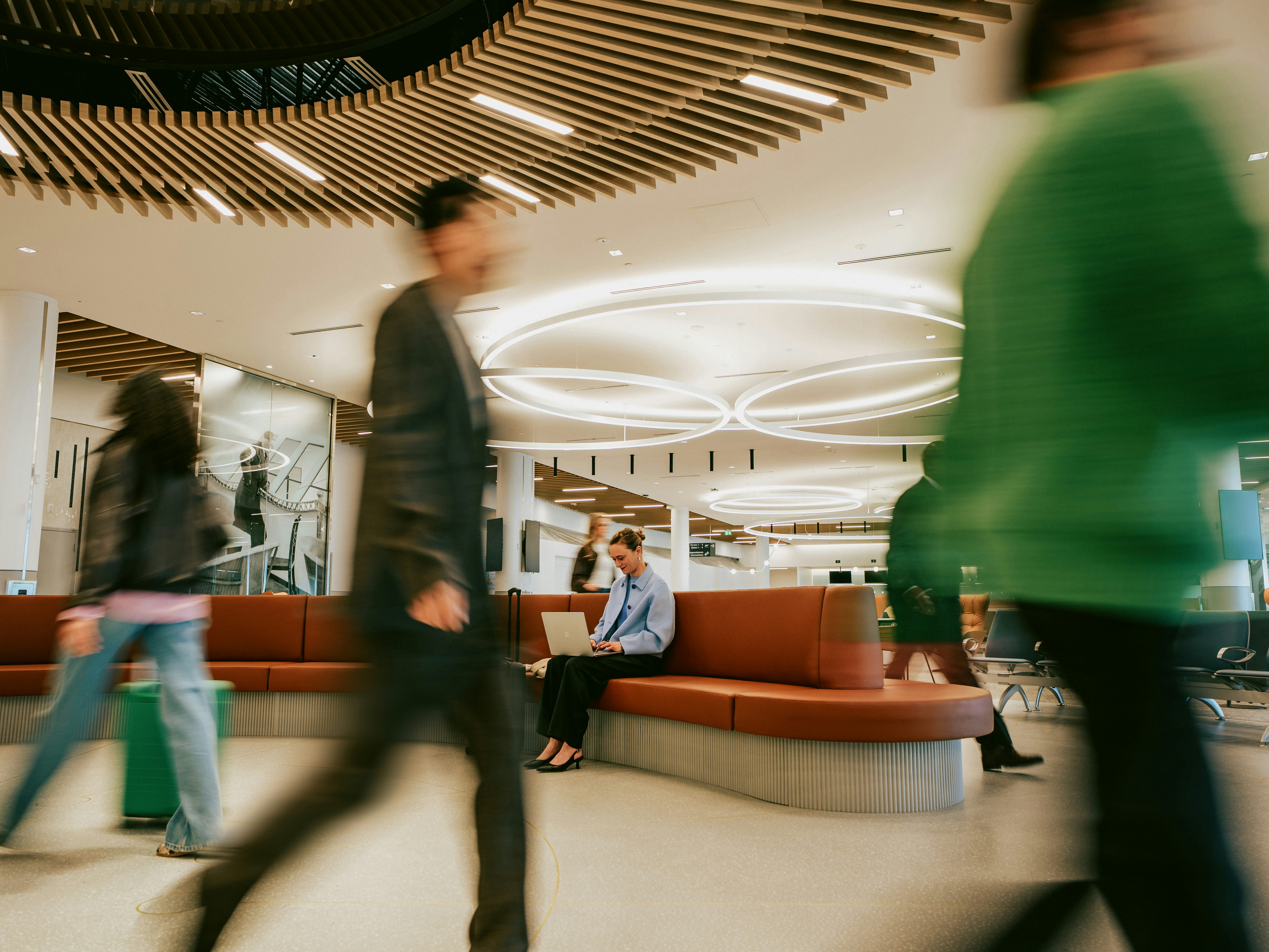 Passagers en mouvement dans l’aire d’attente du terminal du MET, avec voyageuse travaillant sur un ordinateur portable