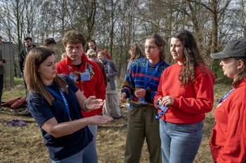 Een kleine groep mensen die buiten staan en luisteren naar iemand die iets uitbeeldt.