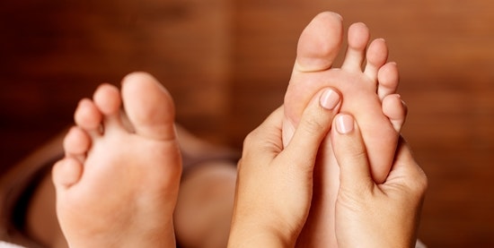 Quelqu'un masse la plante d'un pied avec les deux mains.