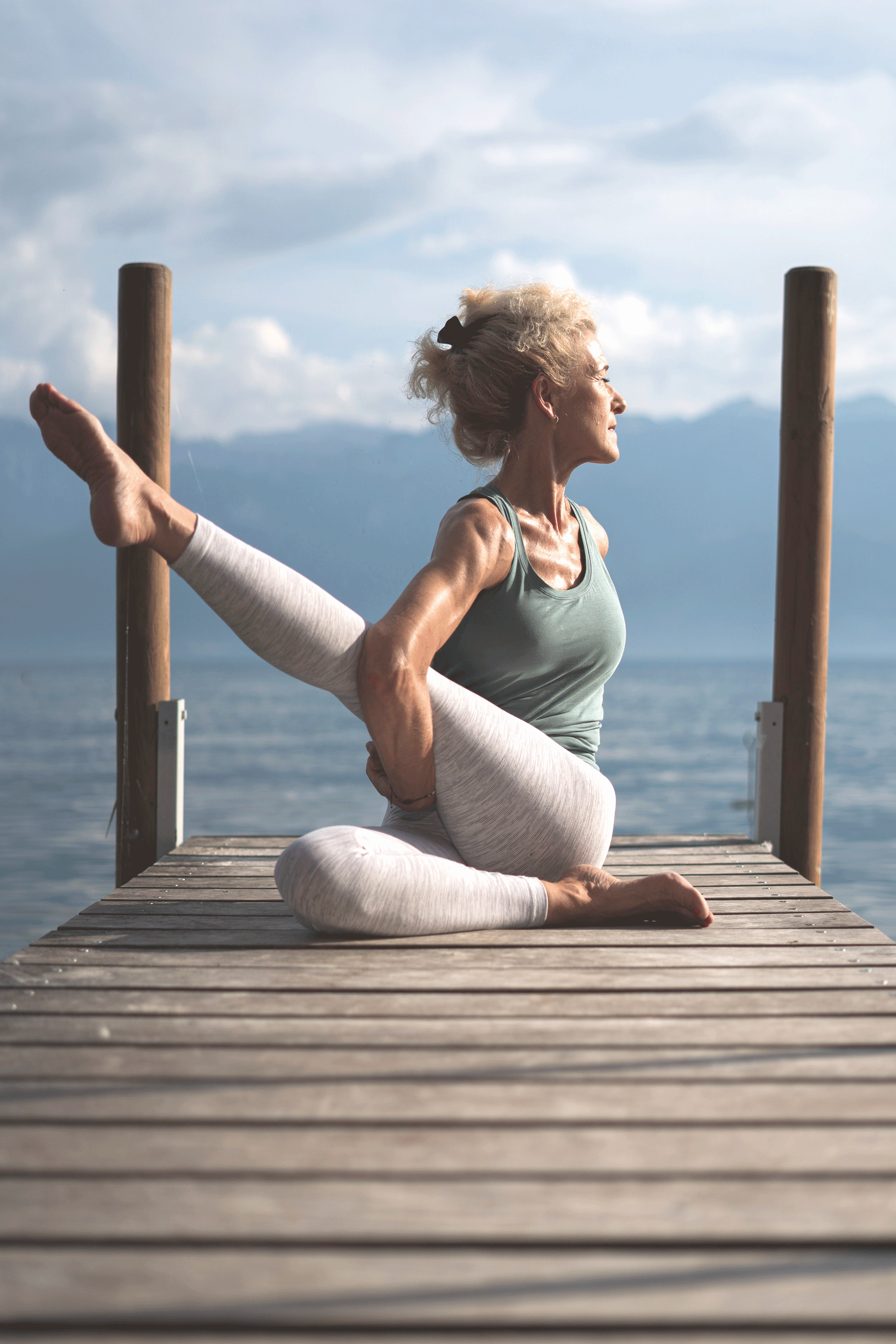 Woman sitting on a pier with her upper body turned, one leg stretched out, arms crossed underneath
