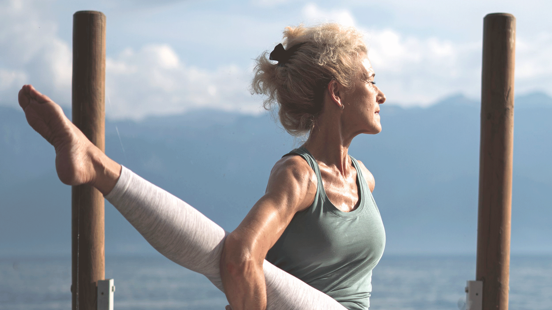 Feel Good Yoga im Hotel Beatus Frau sitzt mit gedrehtem Oberkörpfer auf Schiffsteg, ein Bein gestreckt, die Arme darunter verschränkt
