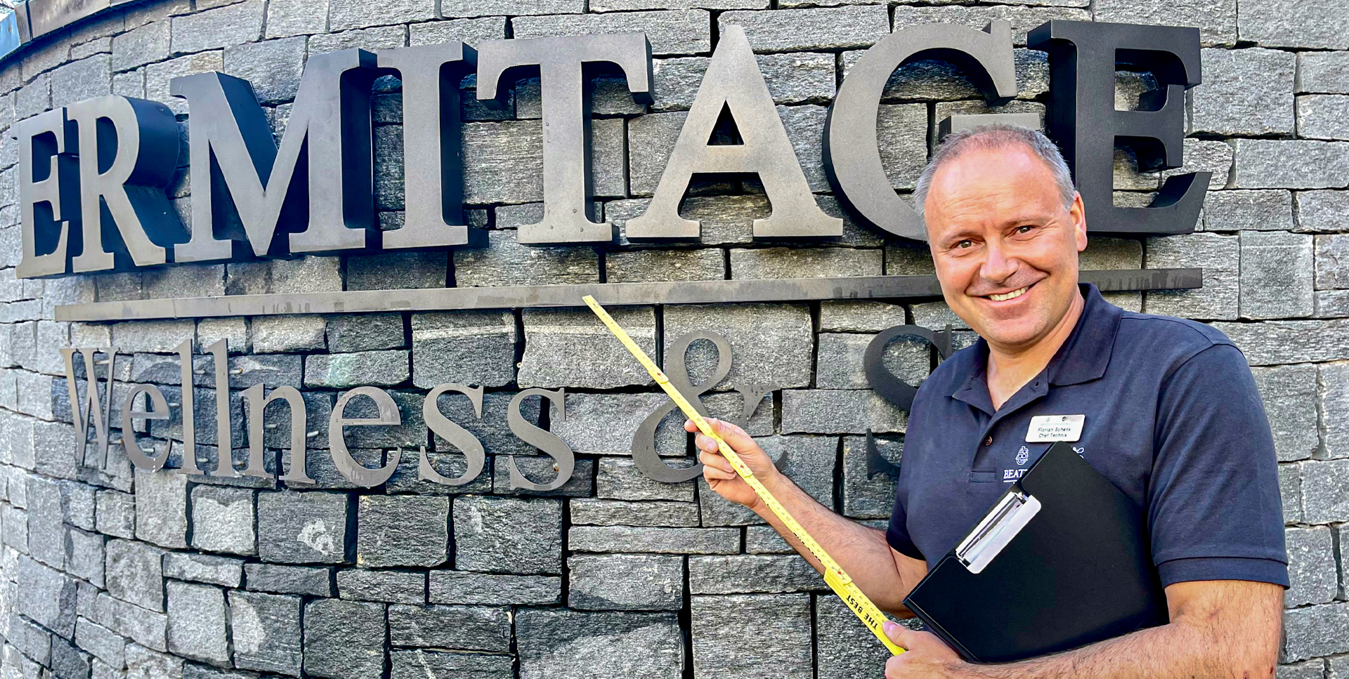 Mann mit Zollstab vor einer Steinwand mit Inschrift Ermitage Wellness & Spa