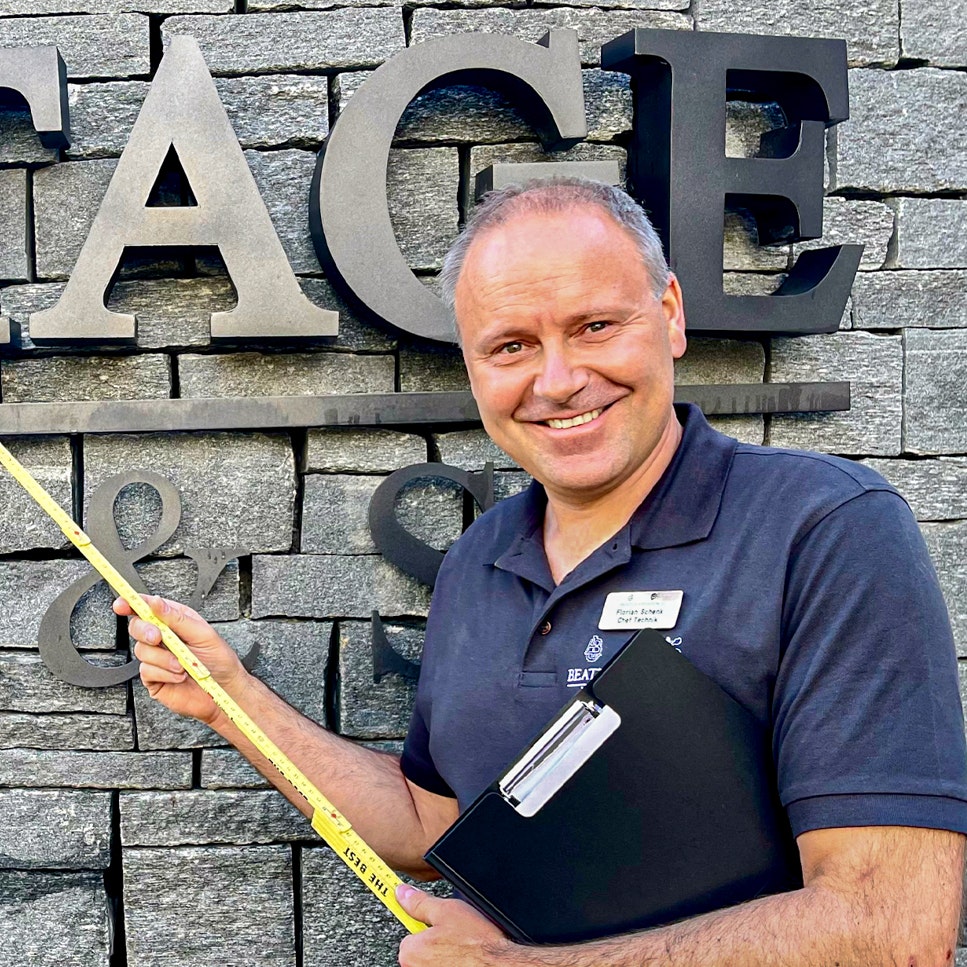 Florian Schenk, chef technique de l'hôtel Ermitage Homme avec un mètre pliant devant un mur de pierre portant l'inscription Ermitage Wellness & Spa