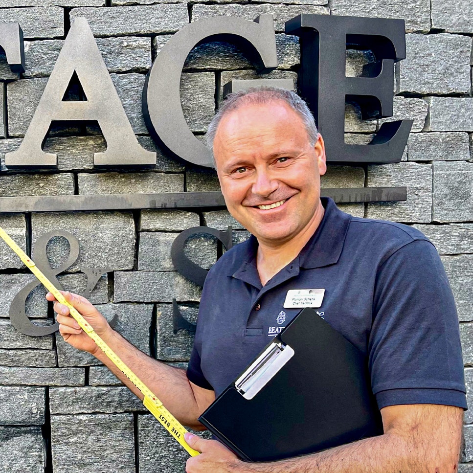 Florian Schenk, Head of Technology at the Hotel Ermitage Man with a folding rule in front of a stone wall with the inscription Ermitage Wellness & Spa