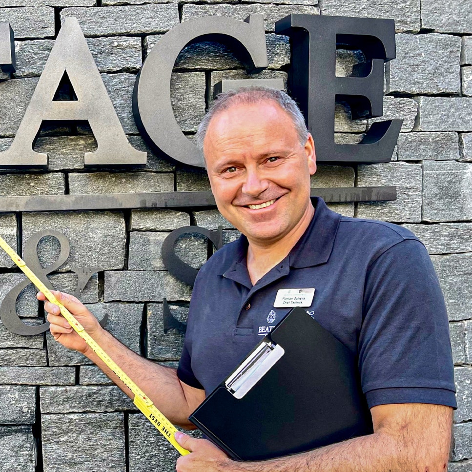 Florian Schenk, Chef Technik im Hotel Ermitage Mann mit Zollstab vor einer Steinwand mit Inschrift Ermitage Wellness & Spa