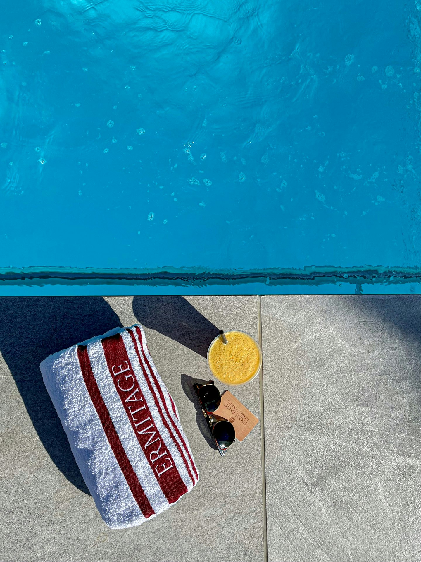 Détail de la photo avec piscine, serviette de bain, lunettes de soleil et jus d'orange vus d'en haut