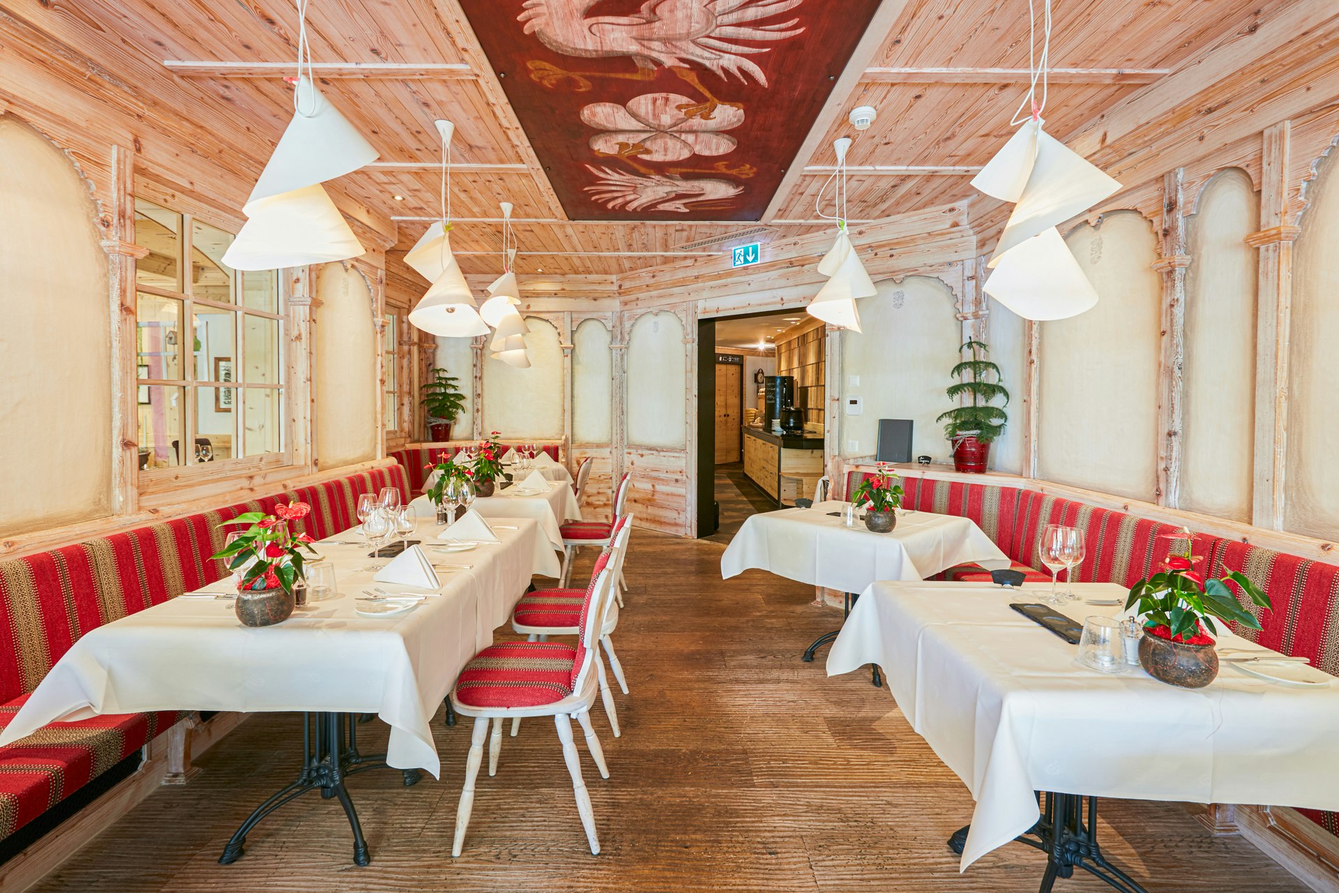 Restaurant avec tables nappées, plafond en bois peint, banquettes et fauteuils recouverts de coussins rouges