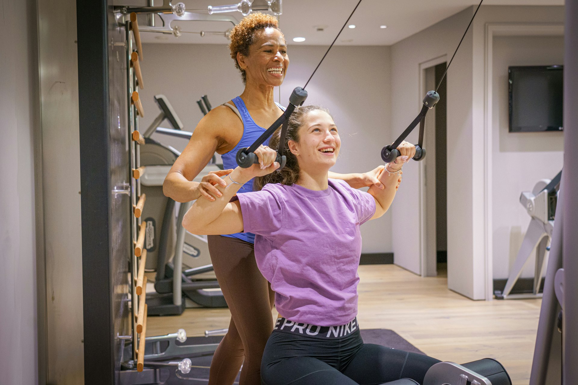 Eine lachende Frau zeigt einer anderen, wie sie die Trainingsgeräte richtig benützt
