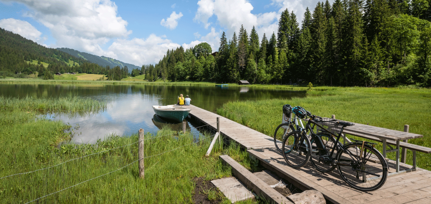 Two people have parked their bikes and are sitting on a wooden jetty by a small natural lake
