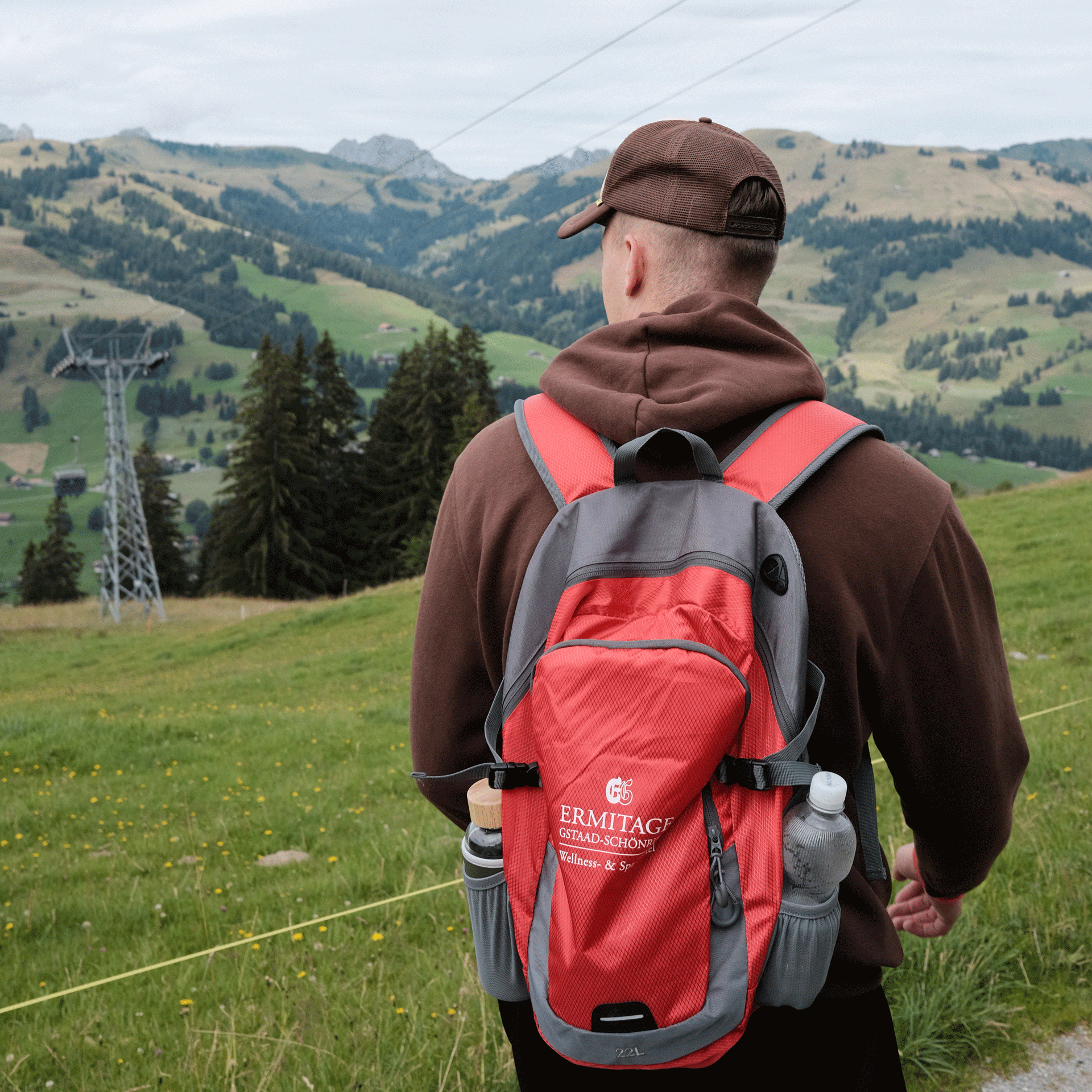 Hiking with the nature guides from the Hotel Ermitage A man with a red Ermitage rucksack in front of a mountain landscape