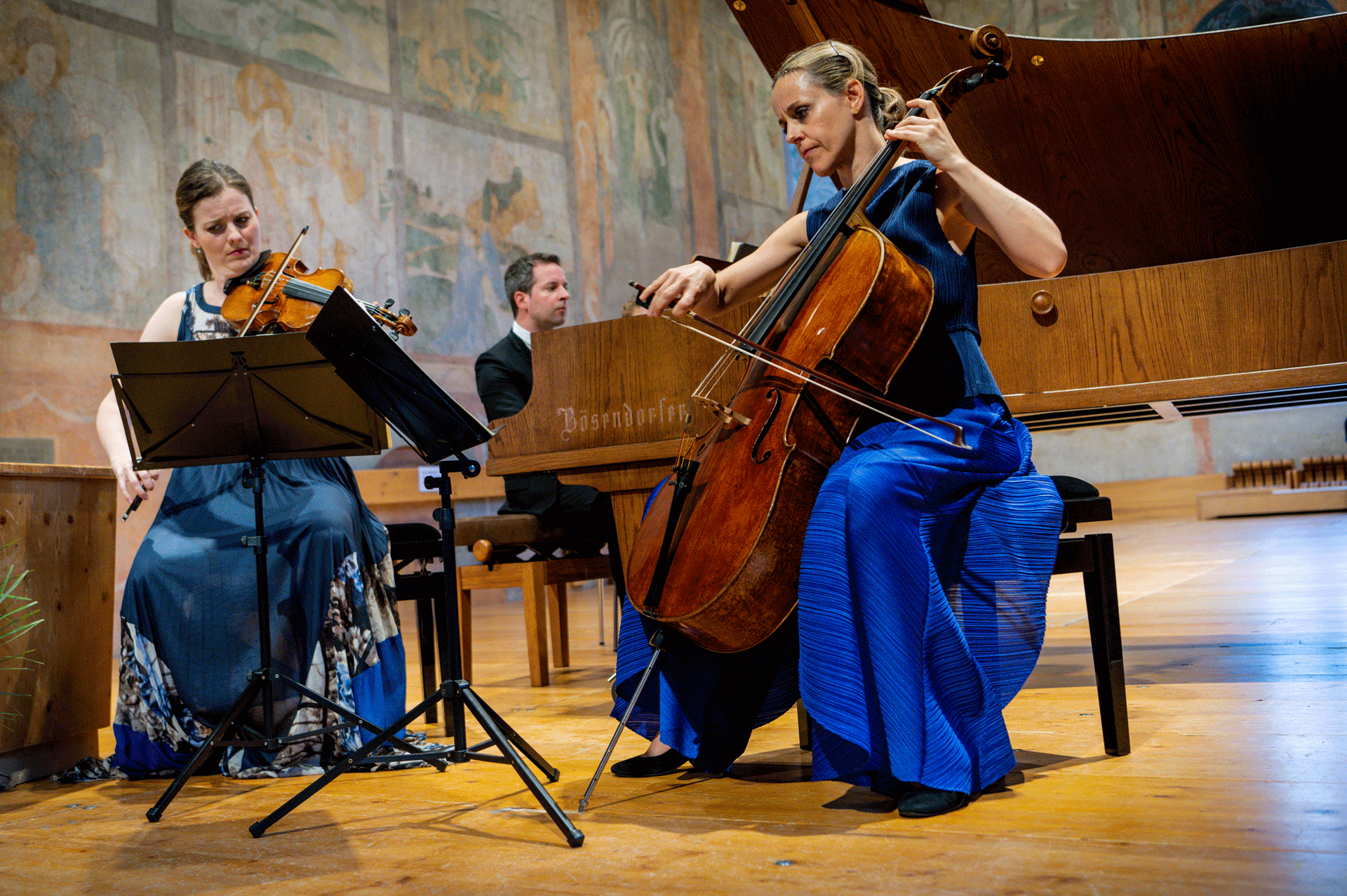 Eine Frau mit Cello und eine mit Geige werden von einem Klavierspieler begleitet