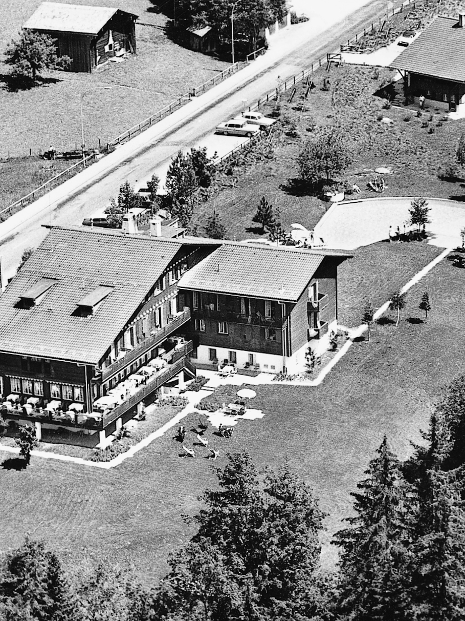Hotel Ermitage 1955 Black and white photo of a wooden house with an extension surrounded by greenery
