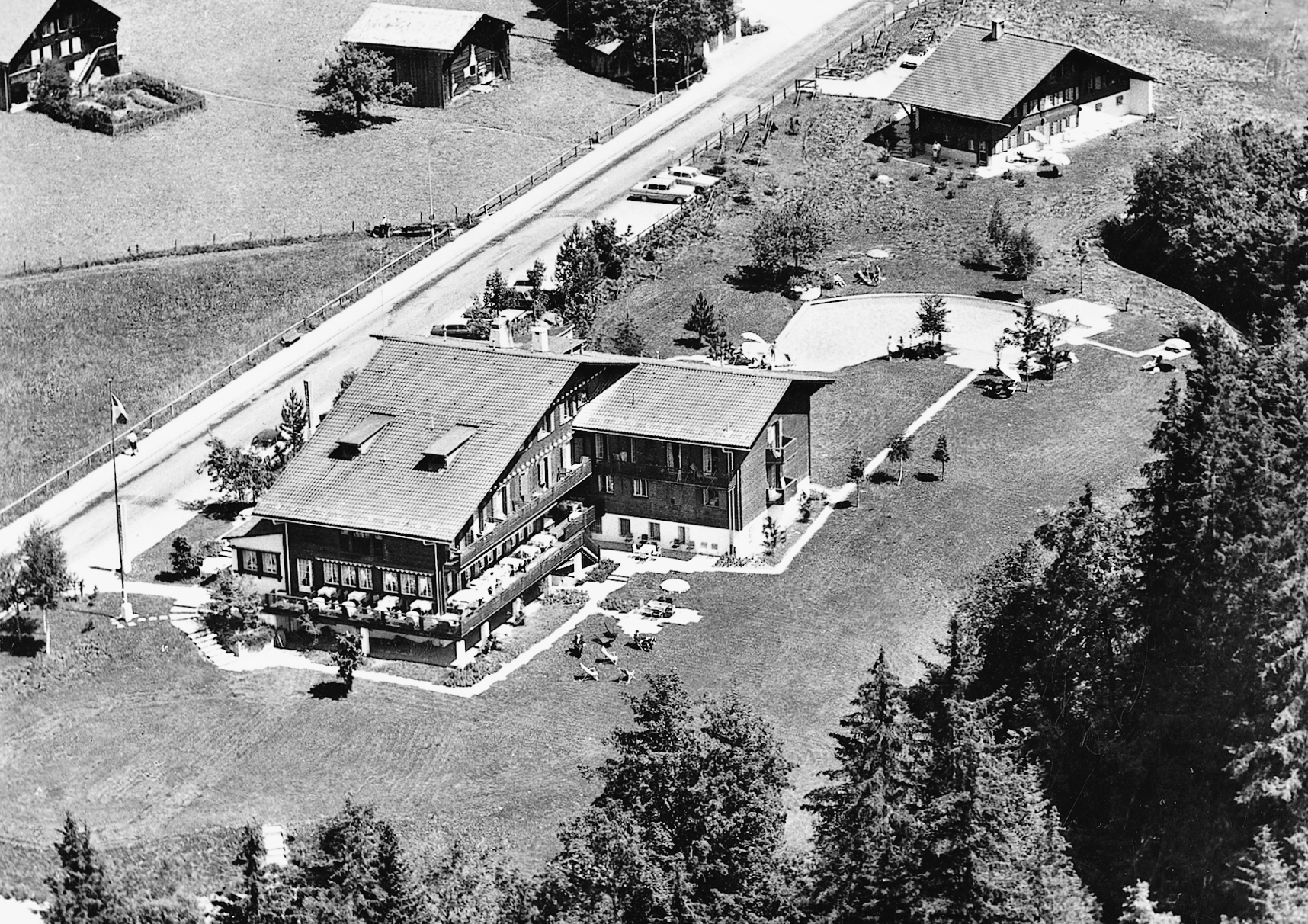 Schwarz-weiss Foto eines Holzhauses mit einem Anbau mitten im Grünen