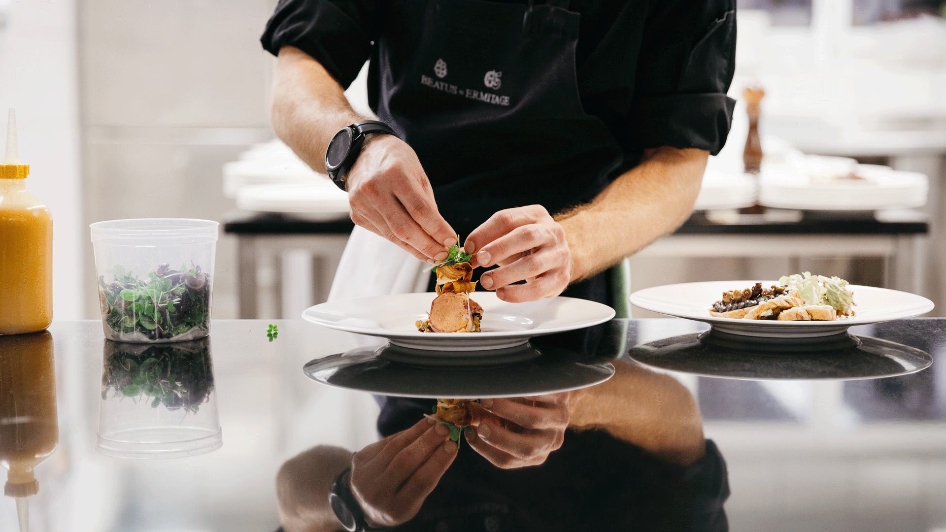 Kitchen at the Hotel Ermitage The hands of a man arranging a dish on a plate