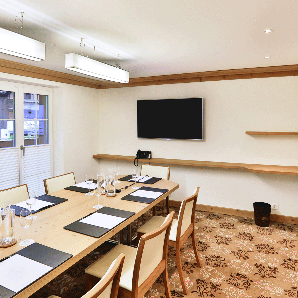 Seminar room at the Hotel Ermitage Room with carpeted floor, neon lights and large table with writing pads and chairs