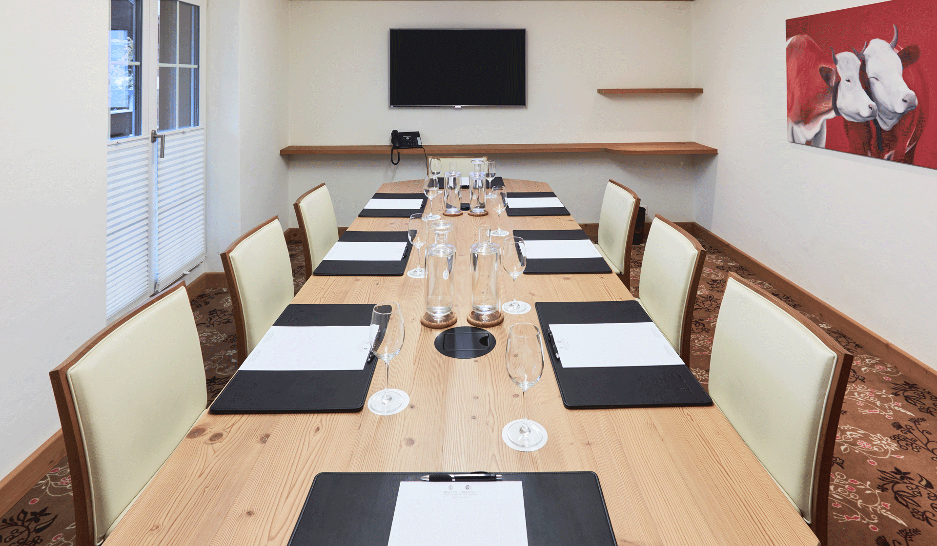 Longue table avec sous-mains et verres, à droite un tableau avec des vaches rouges