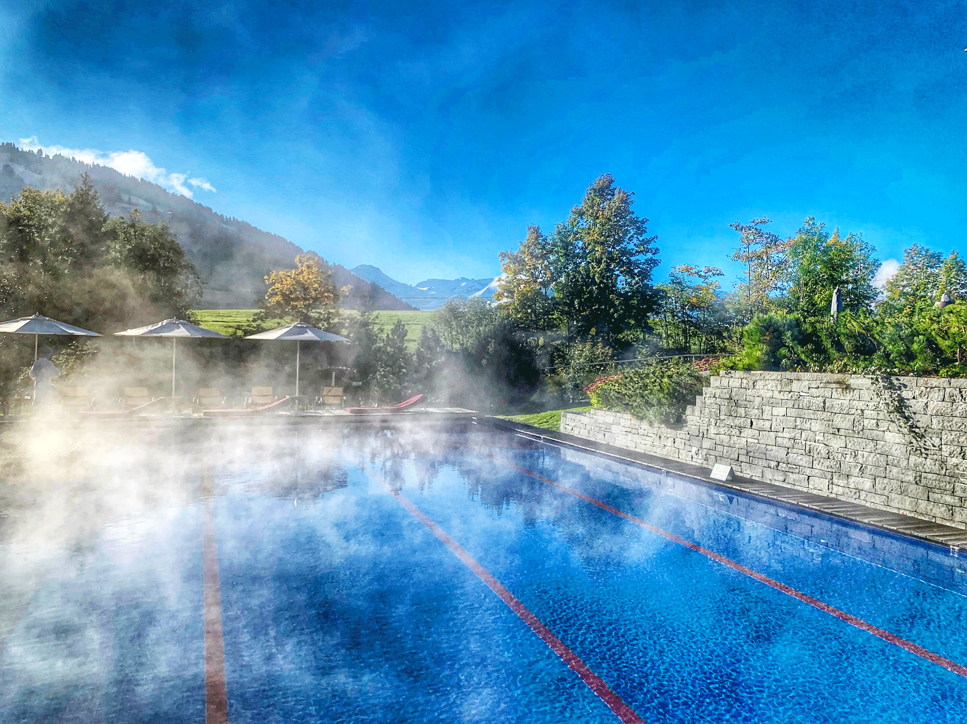 Sportpool mit Längemarkierung, dahinter Liegestühle und Berge