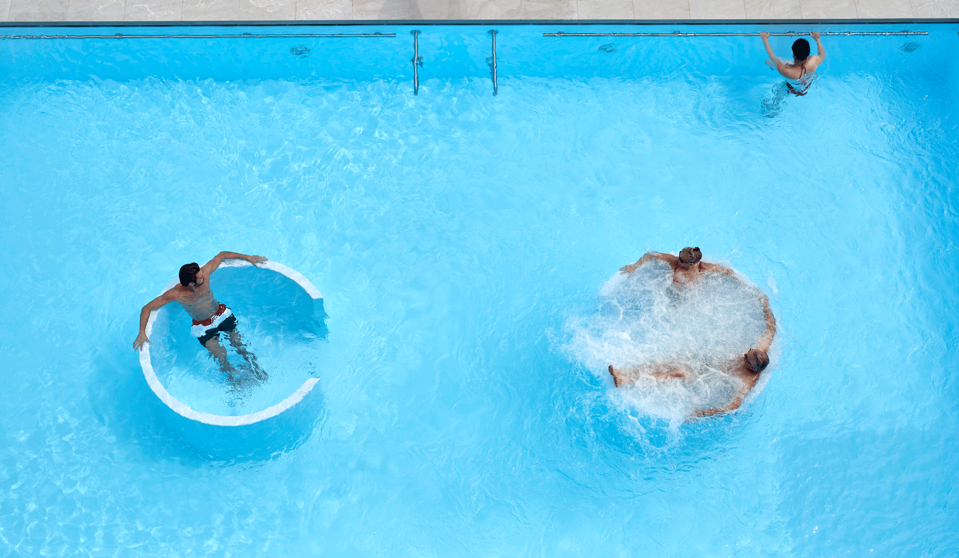 Zwei Sprudelbecken in einem Freibad, darin drei Menschen, von oben gesehen