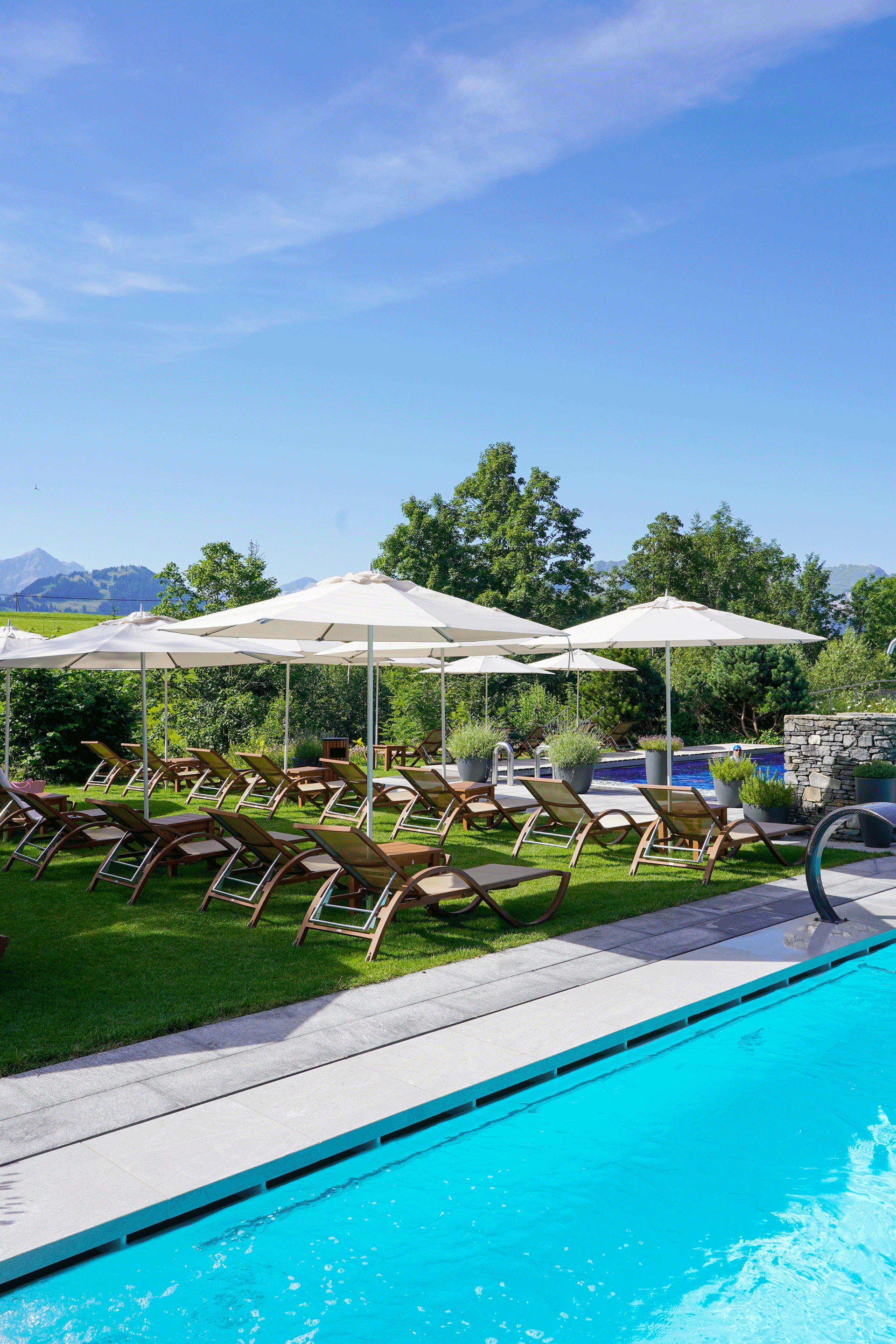 Liegewiese mit Liegestühlen und Sonnenschirmen neben hellblauem Pool