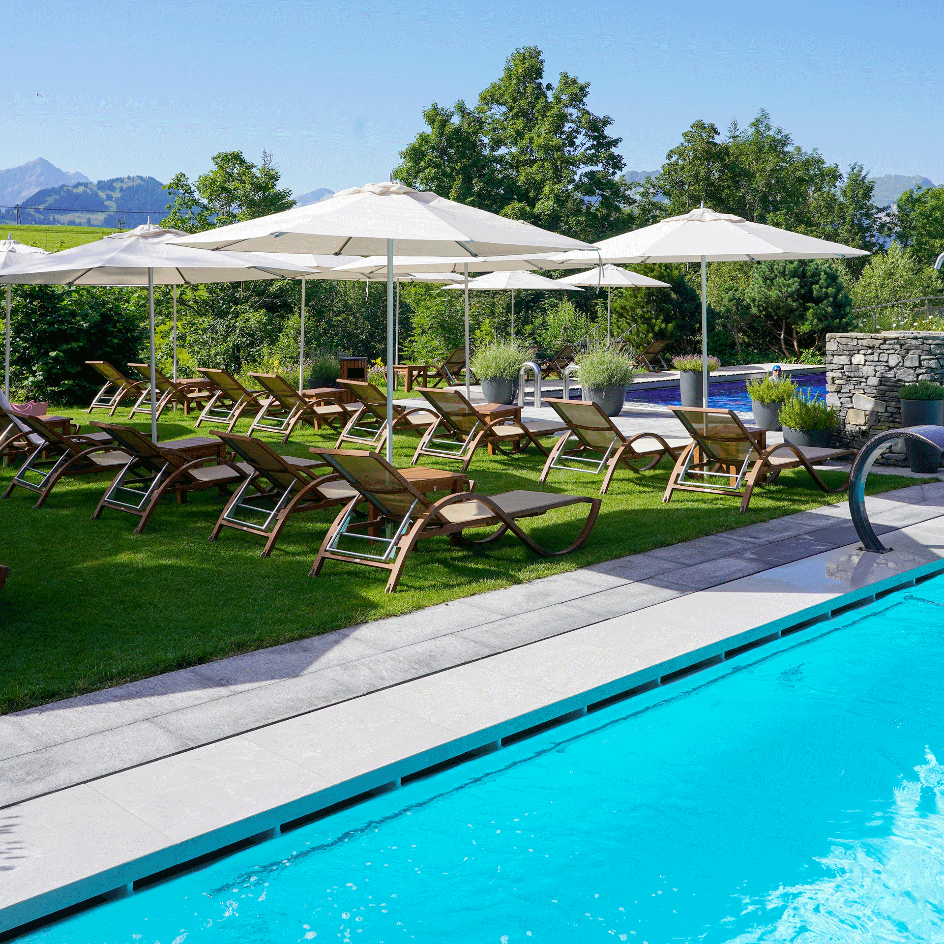 Liegewiese im Hotel Ermitage Liegewiese mit Liegestühlen und Sonnenschirmen neben hellblauem Pool