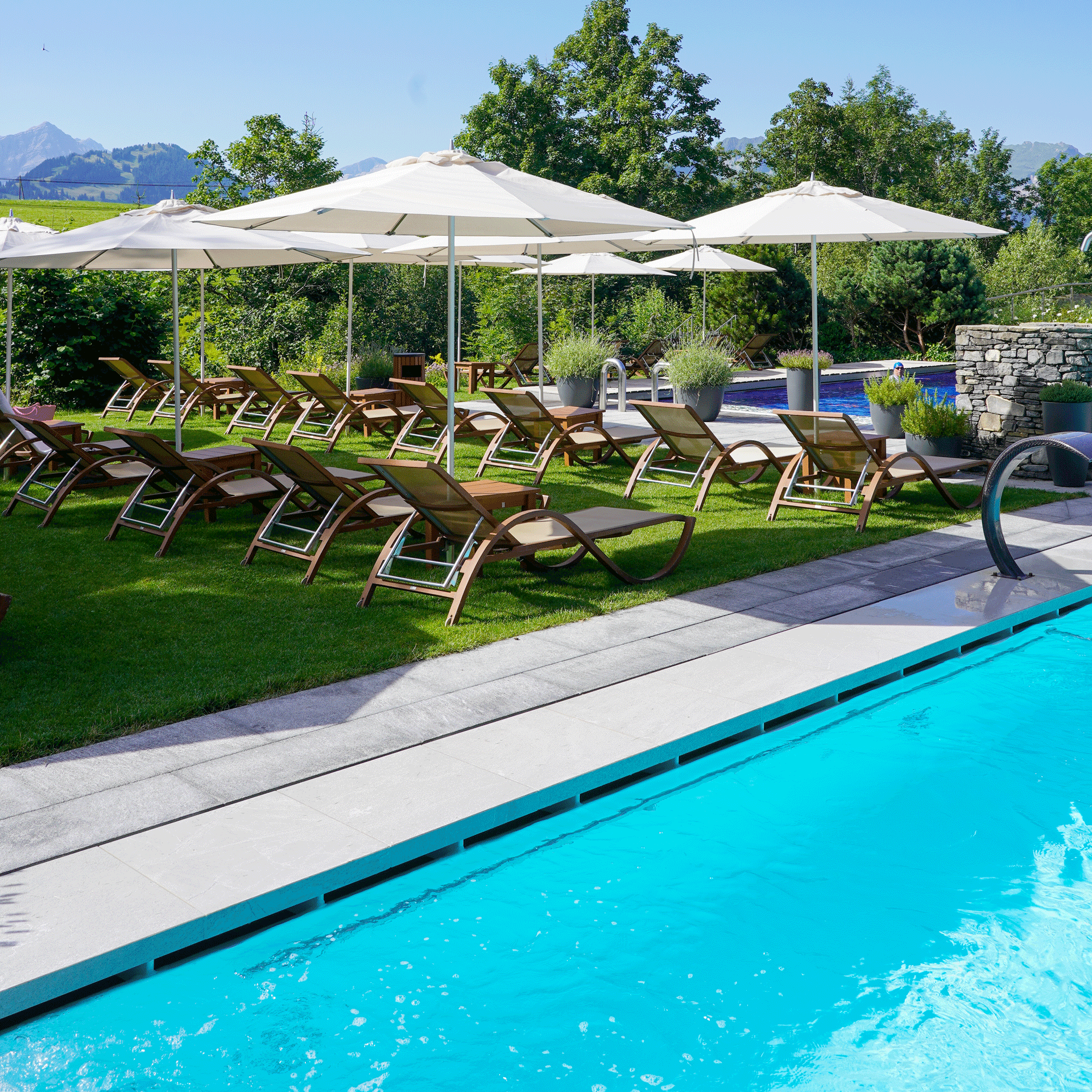 Pelouse de l'hôtel Ermitage Pelouse avec chaises longues et parasols à côté de la piscine bleu clair